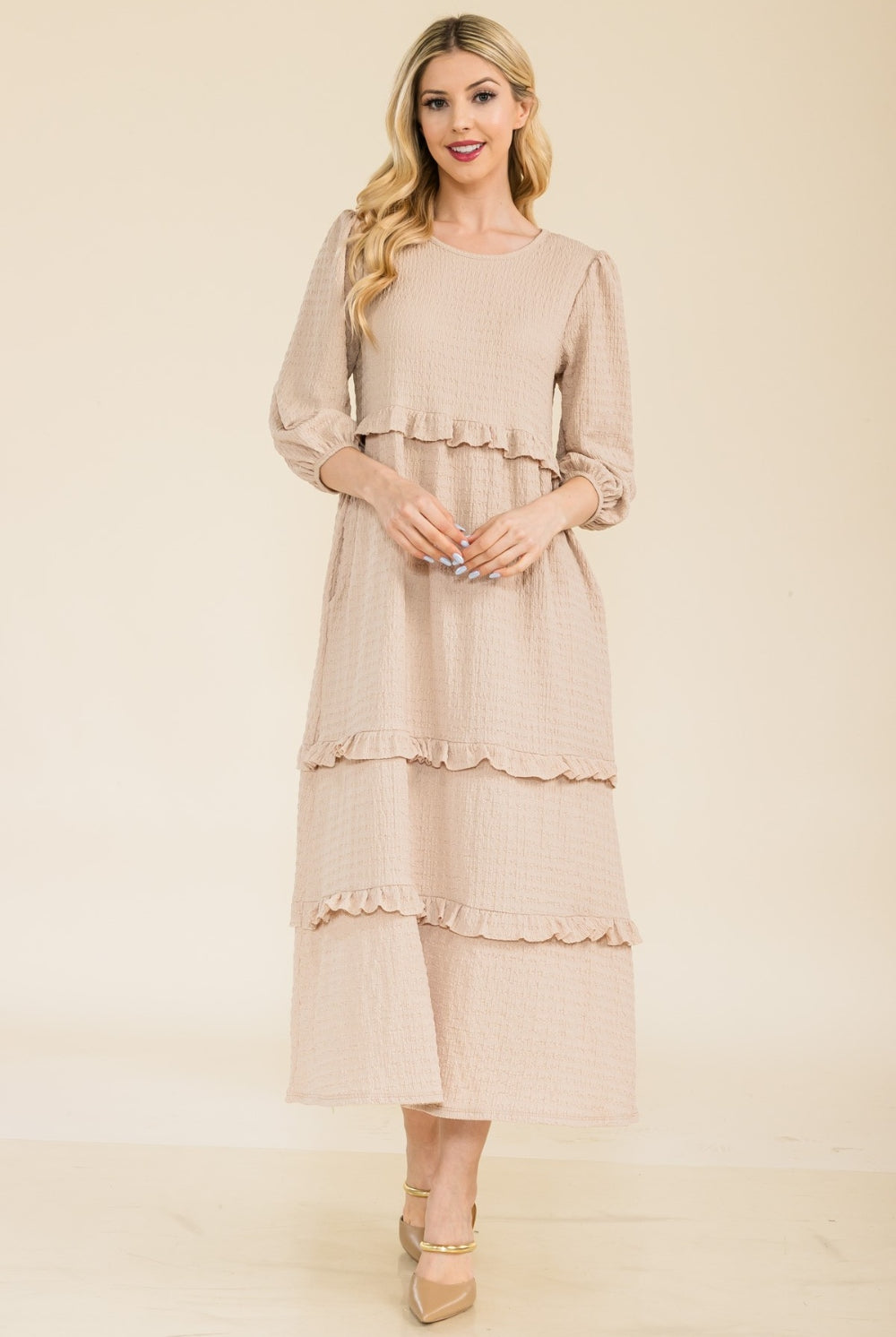 Woman wearing a beige tiered ruffle midi dress with long sleeves.