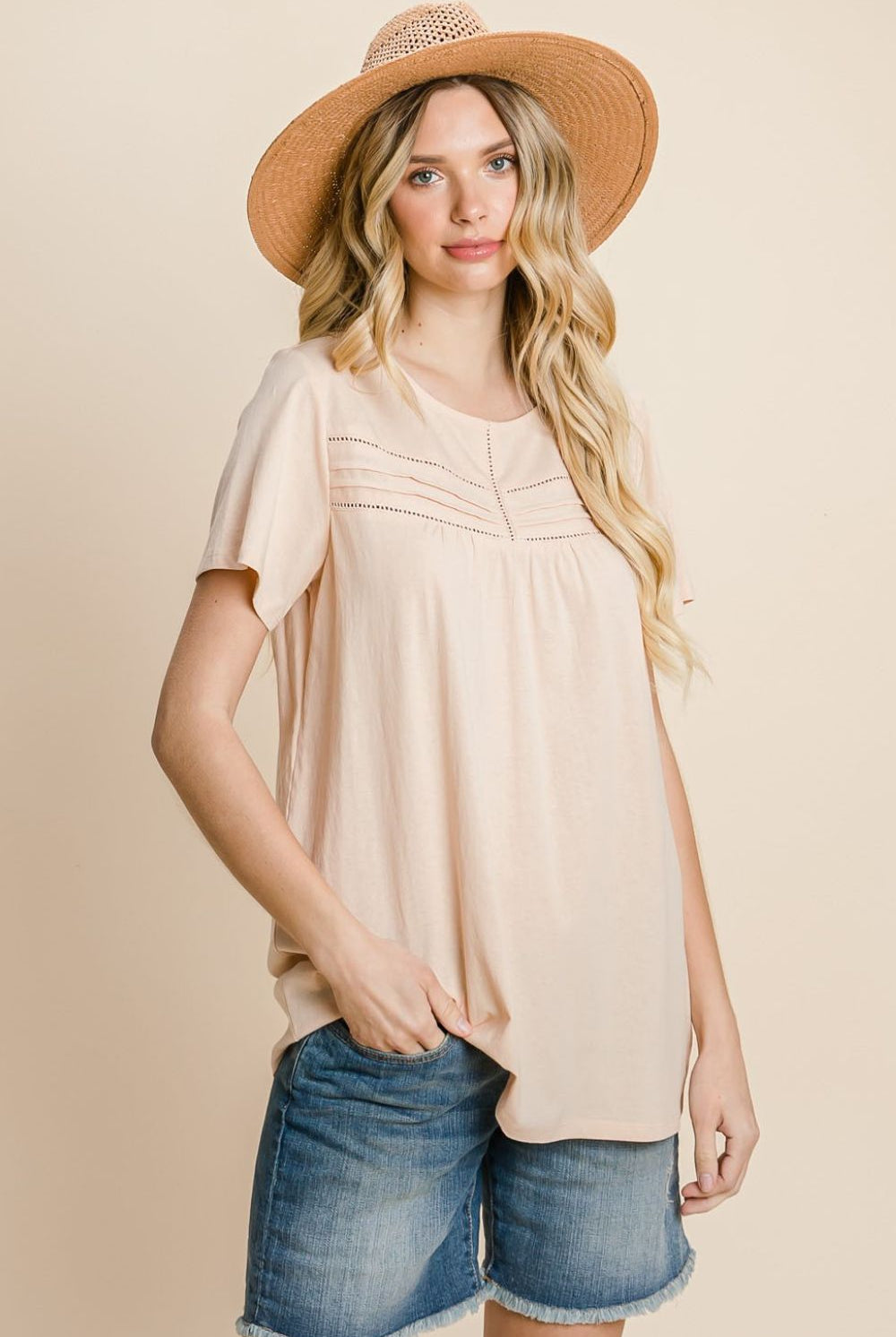 Woman wearing a peach cotton t-shirt with eyelet details, paired with denim shorts and a straw hat.