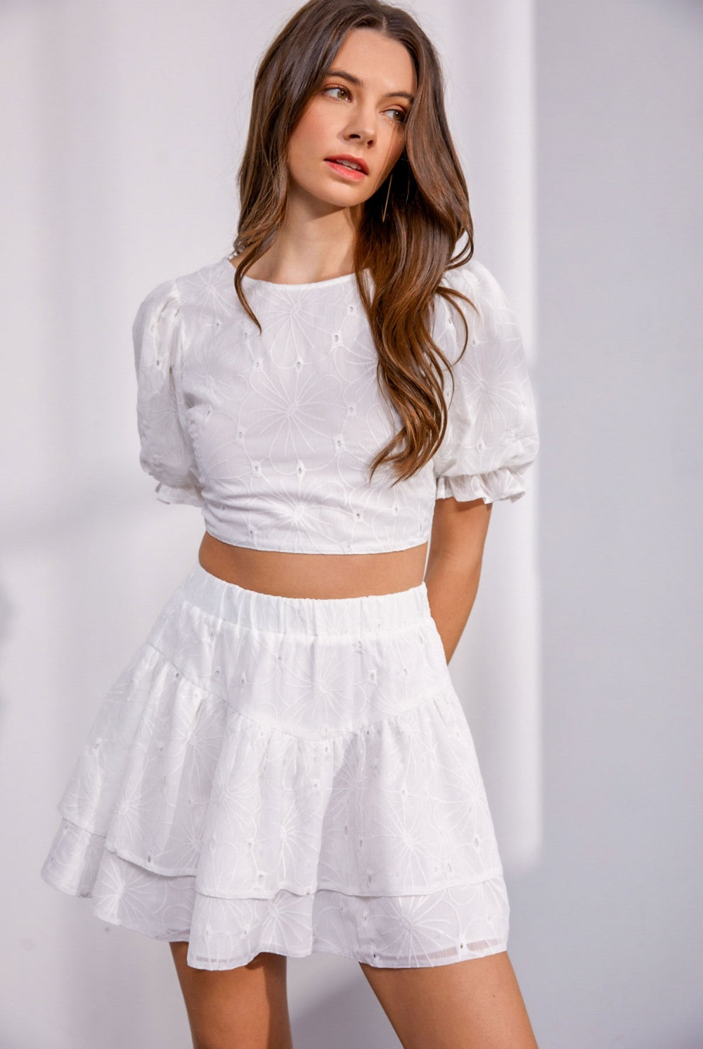 A model wearing a white lace crop top with a floral design, embodying a fresh and feminine style.