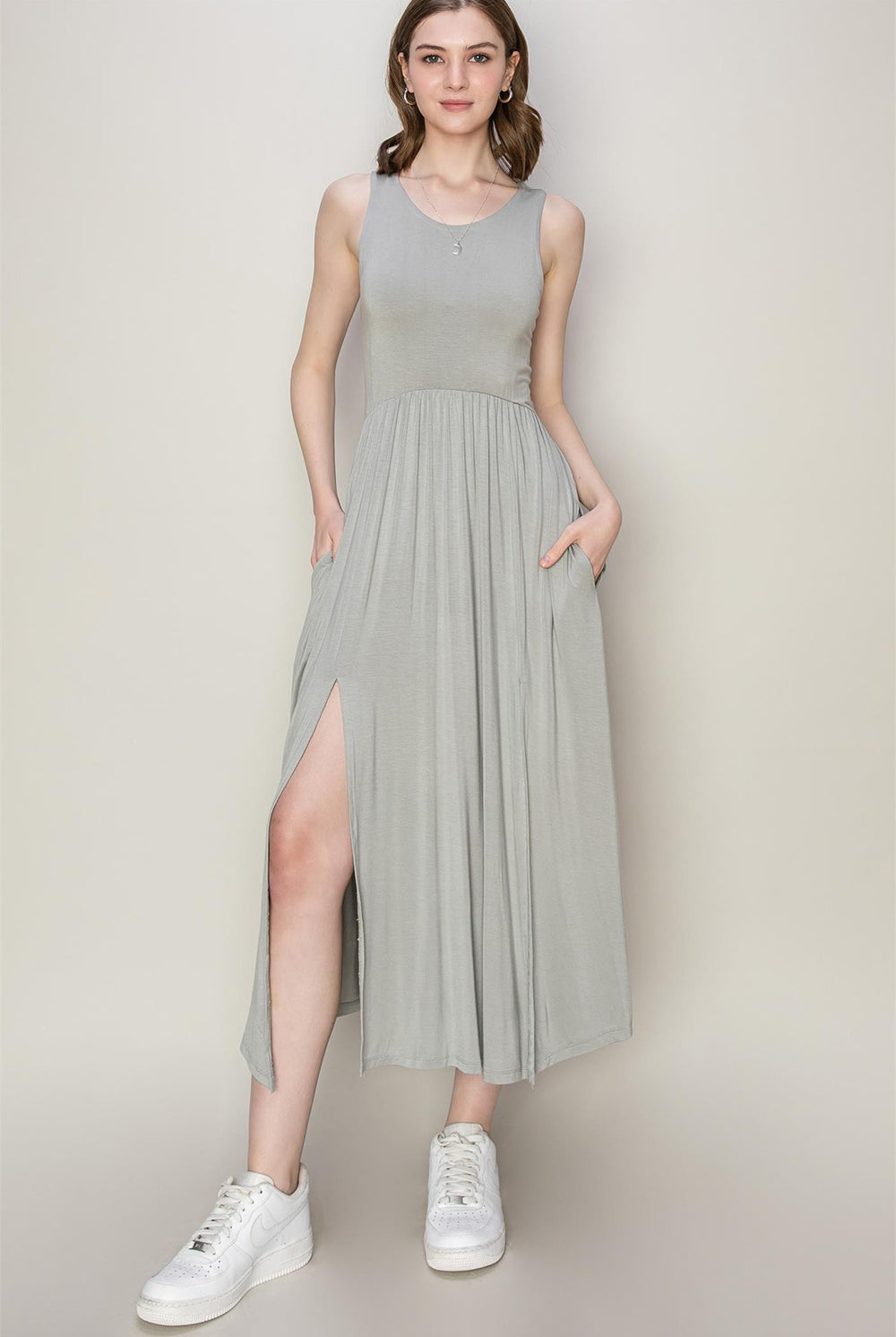 Woman wearing a gray sleeveless midi dress with a slit, paired with white sneakers.