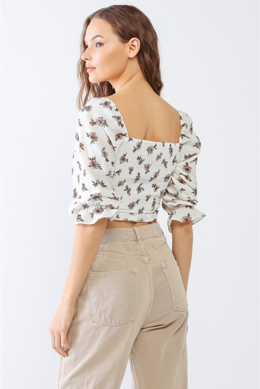 A woman in a white floral ruffled crop top, paired with casual beige pants for a fresh and trendy look.