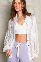 Woman wearing a lace long sleeve button down shirt over a lace crop top, paired with high-waisted pants.