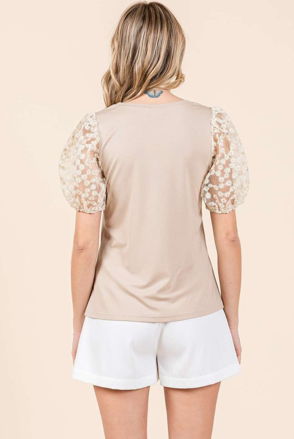A woman wearing a stylish taupe top with puff sleeves, combining modern elegance with classic comfort, perfect for versatile styling.