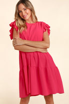 Woman wearing a fuchsia short sleeve ruffle dress with pockets, smiling and posing with arms crossed.