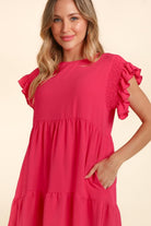 Woman wearing a fuchsia short sleeve ruffle dress with pockets, smiling and posing with arms crossed.