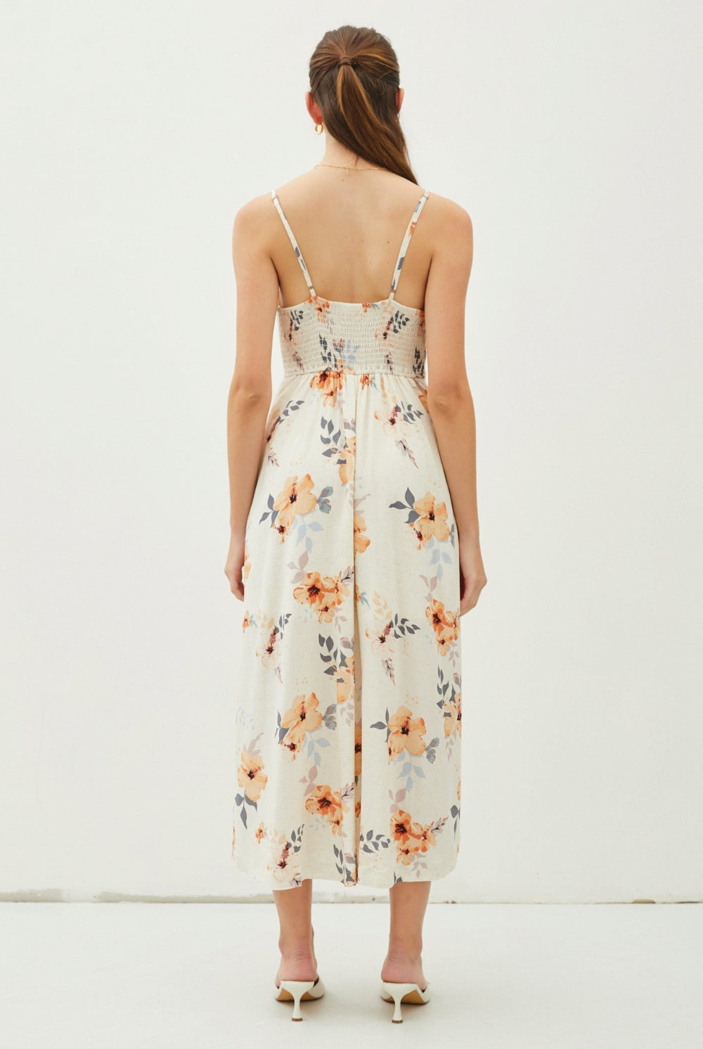 A model is gracefully poised in a botanical print midi dress with a button-front detail, adjustable straps, and a flared skirt, exemplifying casual elegance.