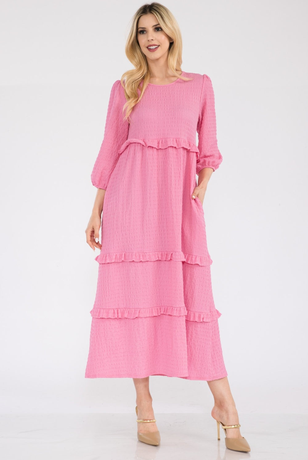 Woman wearing a pink tiered ruffle midi dress with long sleeves.