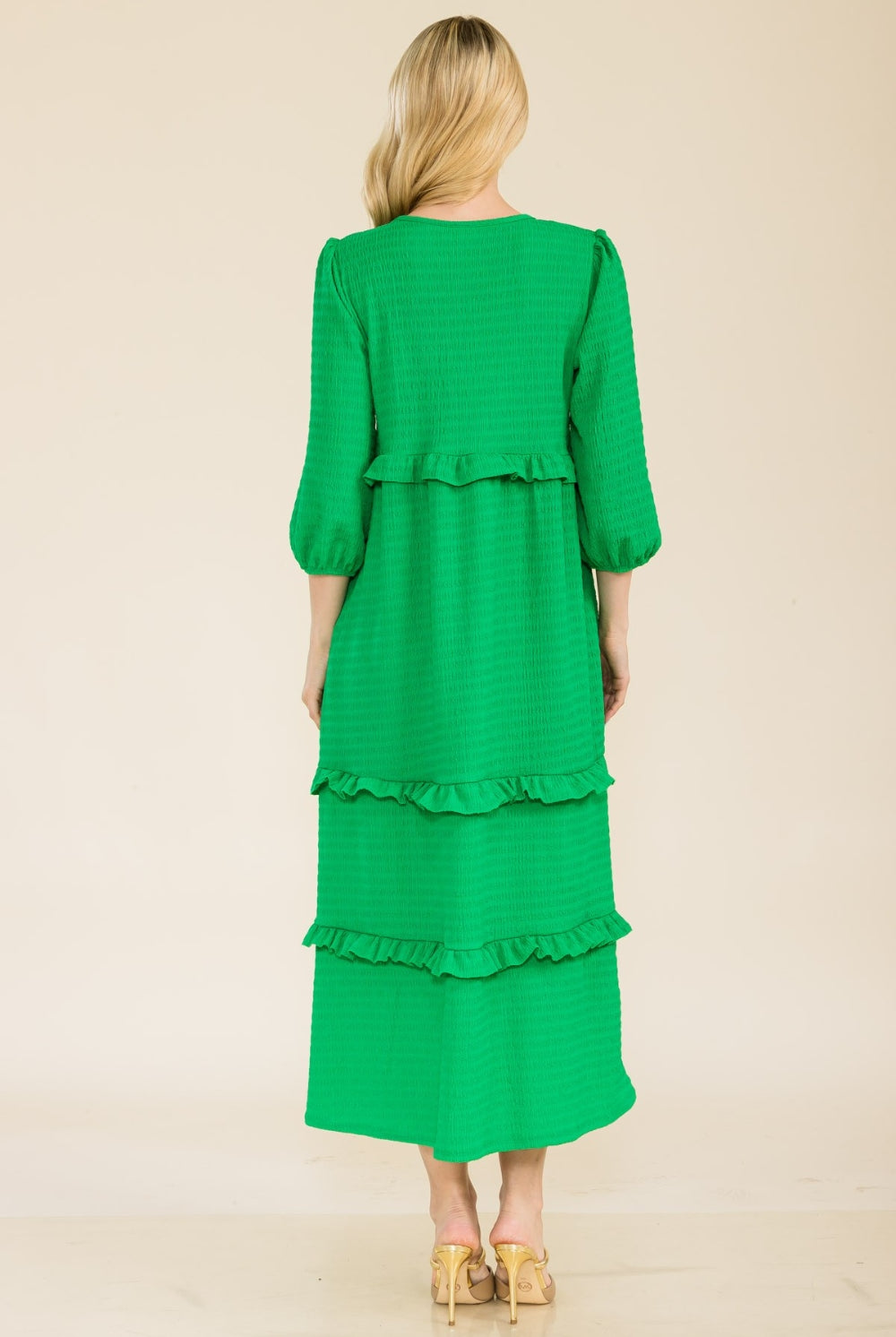 Woman wearing a green tiered ruffle midi dress with long sleeves.