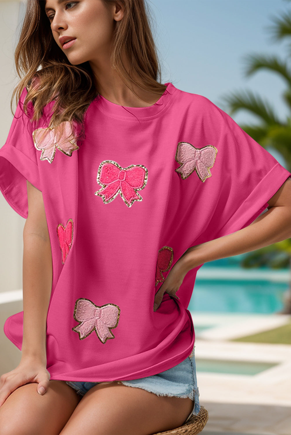 Three images of a woman wearing a sequin bow appliqué t-shirt, available in pink, white, and purple. Each shirt features decorative sequin bows, styled casually with denim shorts and worn by the model in a sunny, poolside setting.