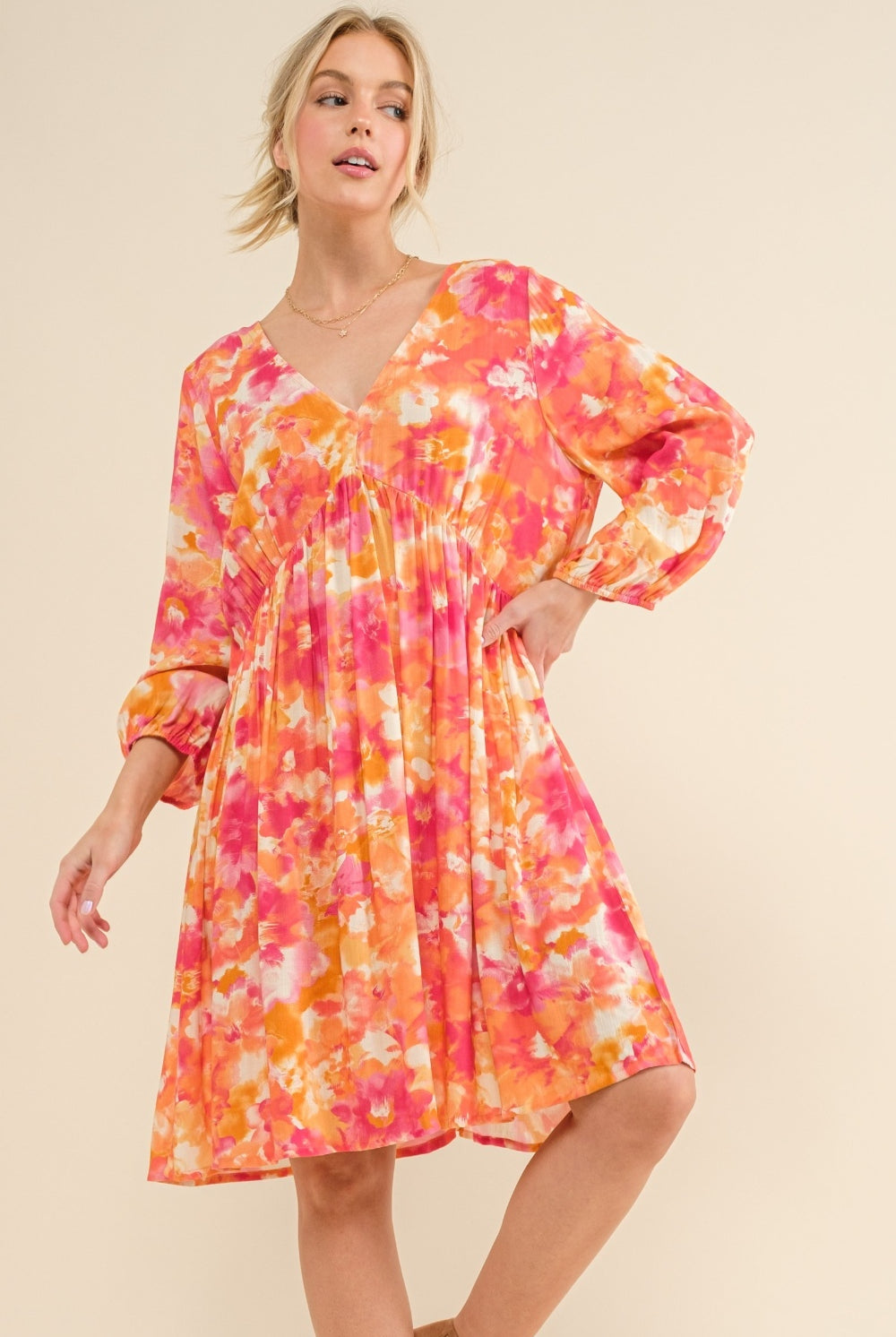 Woman wearing a vibrant floral print long sleeve dress in shades of orange and pink, featuring a tie back detail.