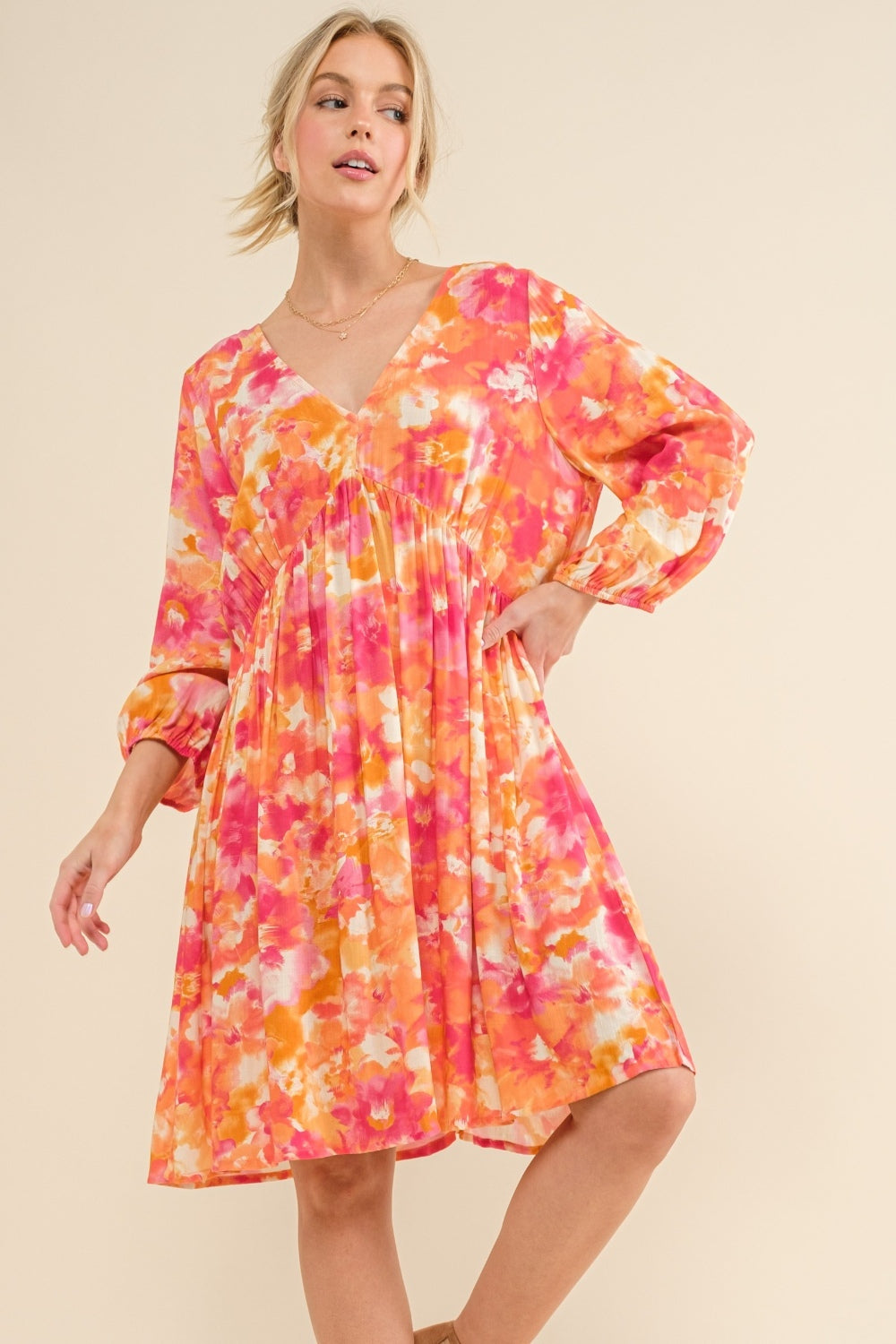 Woman wearing a vibrant floral print long sleeve dress in shades of orange and pink, featuring a tie back detail.