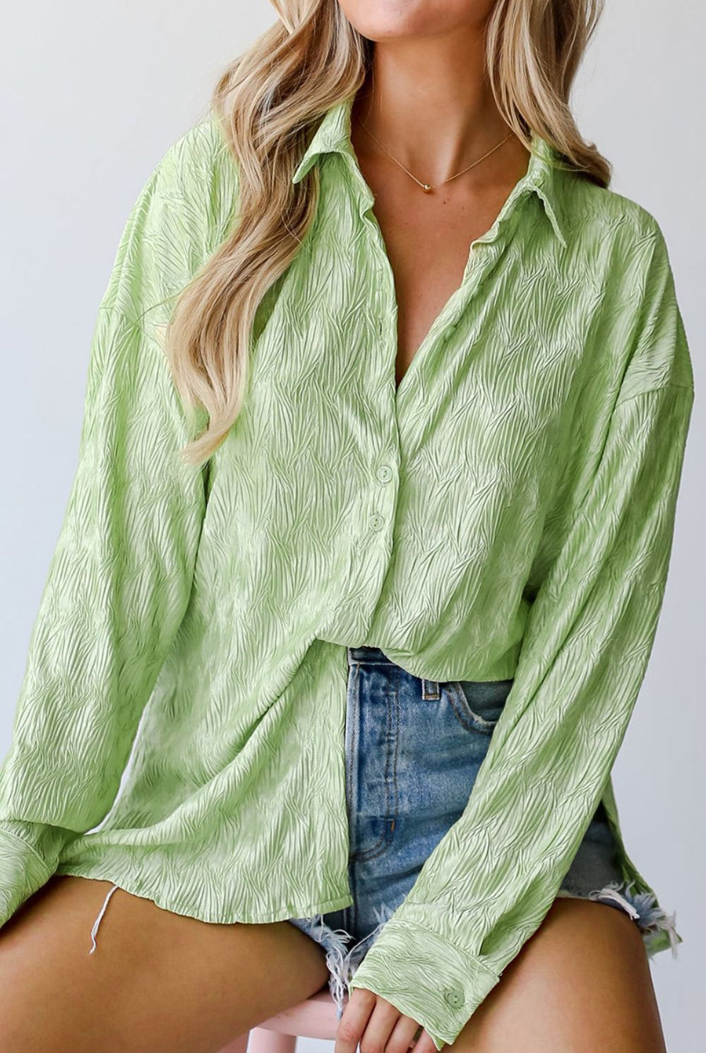 A light green, long-sleeve shirt with a distinctive textured pattern, offering a button-down front and a casual fit. Worn by a woman with blonde hair, it's styled with denim shorts, with the photo capturing from the waist up.
