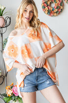 Woman wearing an orange V-neck floral checkered T-shirt, paired with denim shorts for a chic summer look.