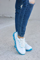 White athletic shoes with vibrant blue accents and transparent air-cushioned soles, paired with classic blue jeans, showcased on a concrete surface.