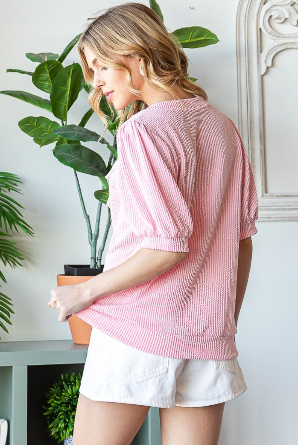 A poised woman in a sweet pink striped half sleeve top with a white bow accent, paired with white shorts, creating a fresh and stylish ensemble perfect for a sunny day.