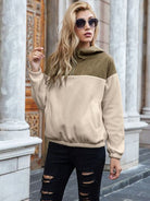 Woman in a stylish quarter-zip color-block hoodie and distressed jeans, accessorized with sunglasses and open-toe sandals, posing in an urban setting.