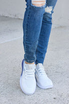 White and light blue athletic shoes with a translucent blue bubble sole, paired with blue cuffed jeans, on a concrete surface.