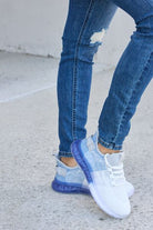 White and light blue athletic shoes with a translucent blue bubble sole, paired with blue cuffed jeans, on a concrete surface.