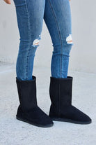 A pair of classic black mid-calf boots paired with distressed blue denim jeans, showcased on a plain concrete surface.