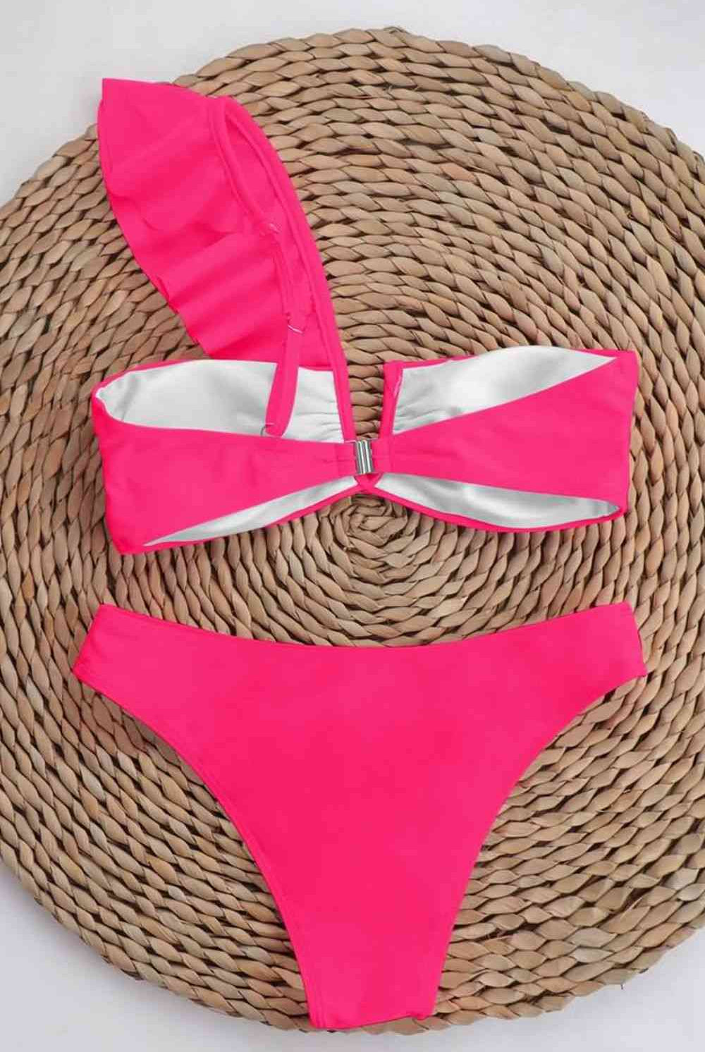Smiling woman by the pool in a vibrant pink ruffled one-shoulder bikini top and matching low-rise bikini bottoms.