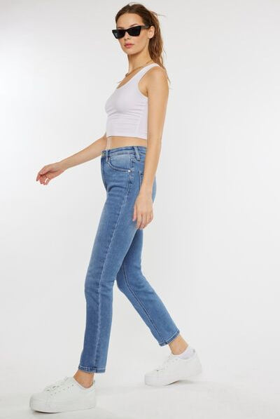 A model styled in casual attire, featuring cat whiskers high-waist jeans in light blue, complemented with a cropped white tank top, a black zip-up jacket, and white sneakers, exuding a relaxed and trendy vibe.