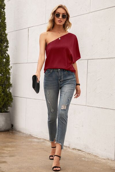 Elegant one-shoulder top available in black, burgundy, royal blue, and beige, styled with classic denim for a versatile look.