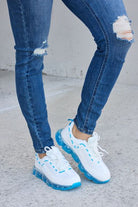 White athletic shoes with vibrant blue accents and transparent air-cushioned soles, paired with classic blue jeans, showcased on a concrete surface.