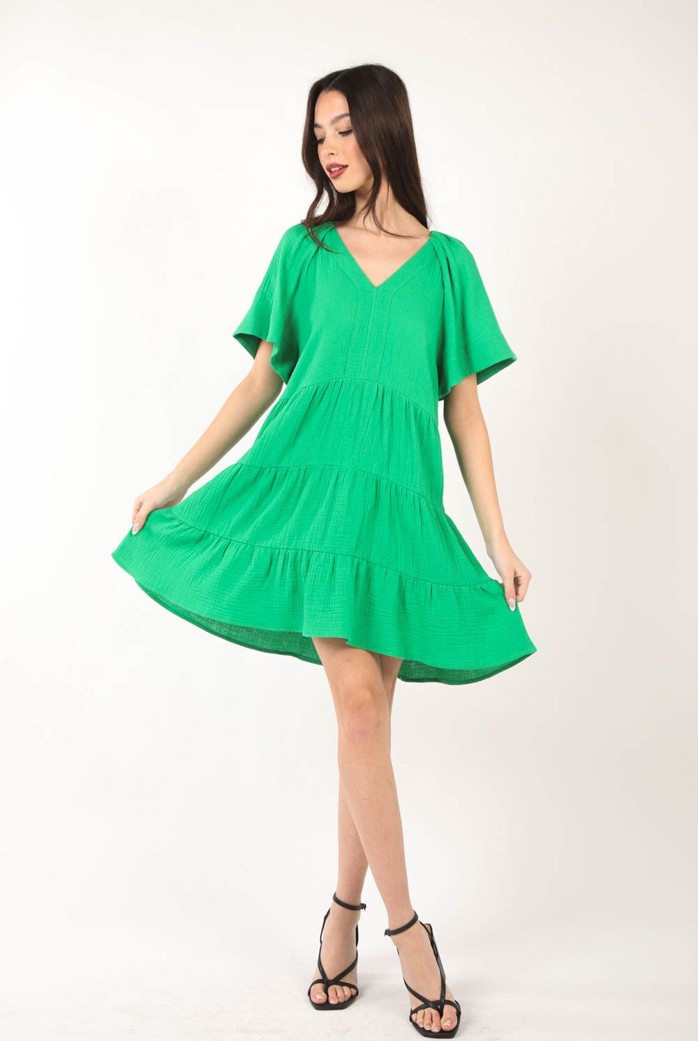 Model wearing a vibrant green, tiered dress with a V-neckline and short sleeves, perfect for a fresh and stylish summer look.