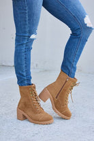 Tan lace-up ankle boots with chunky heels and side zippers, paired with ripped blue skinny jeans, on a concrete background.