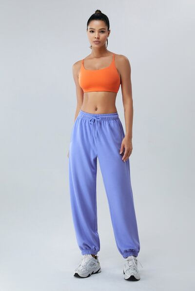 Confident model wearing the Sunset Orange VersaFit Sports Bra, featuring a comfortable fit and vibrant color, paired with relaxed light blue joggers.