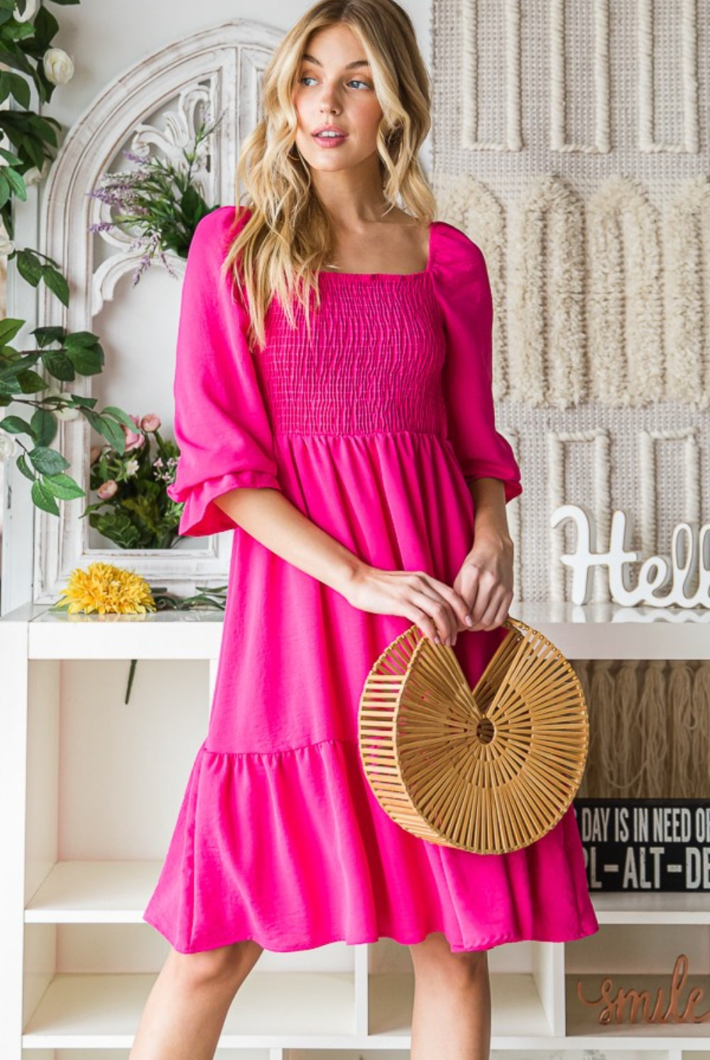 A stylish woman poses in a vibrant pink smocked ruffle hem dress, holding a trendy bamboo circle bag, creating an effervescent and fashion-forward summer outfit.