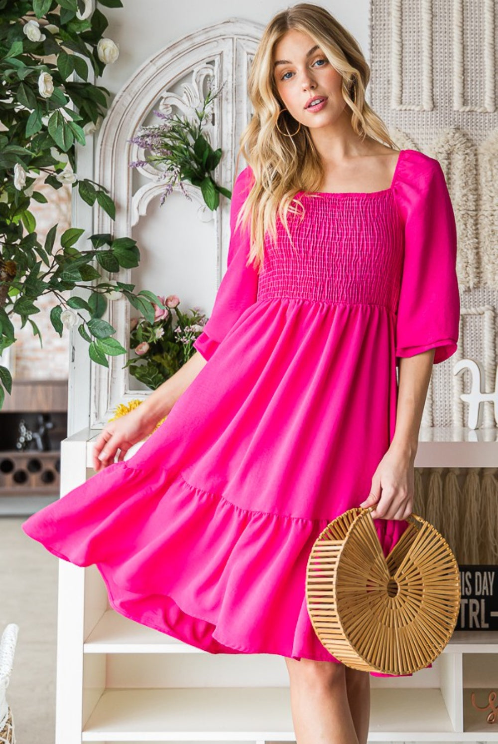 A stylish woman poses in a vibrant pink smocked ruffle hem dress, holding a trendy bamboo circle bag, creating an effervescent and fashion-forward summer outfit.