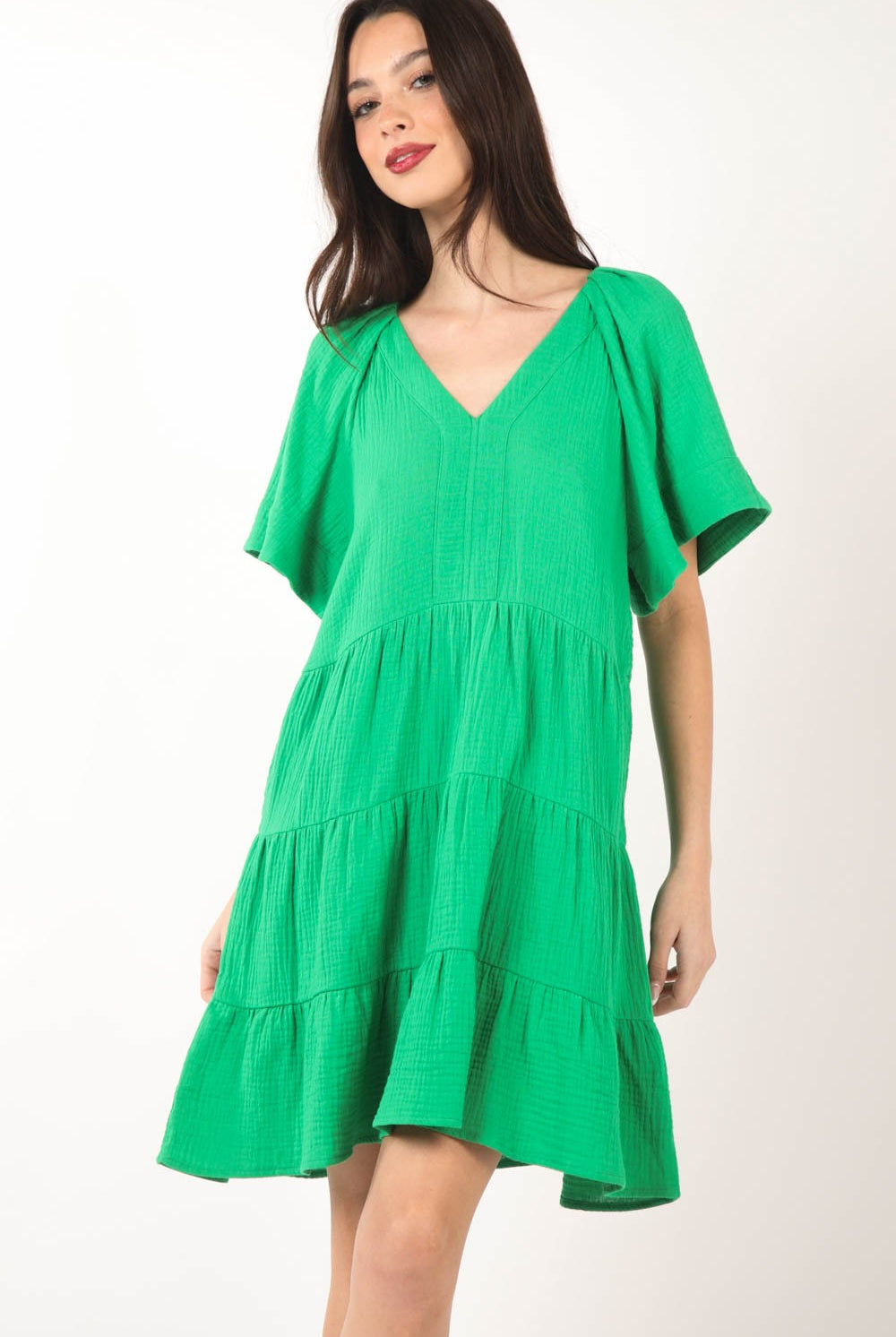 Model wearing a vibrant green, tiered dress with a V-neckline and short sleeves, perfect for a fresh and stylish summer look.